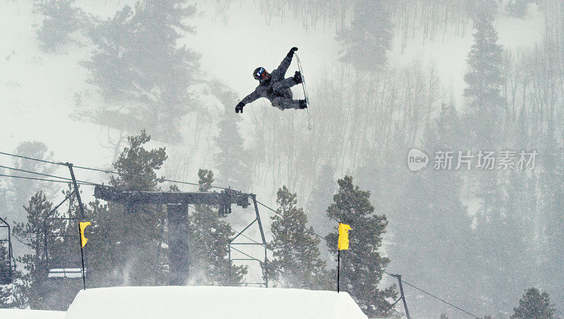 一个滑雪板在完整的冬季装备尝试一个“背部Rodeo 720鼻子抓取”的跳跃与森林和滑雪跳跃的背景在埃尔朵拉滑雪度假村附近，科罗拉多州在一个下雪的，阴天